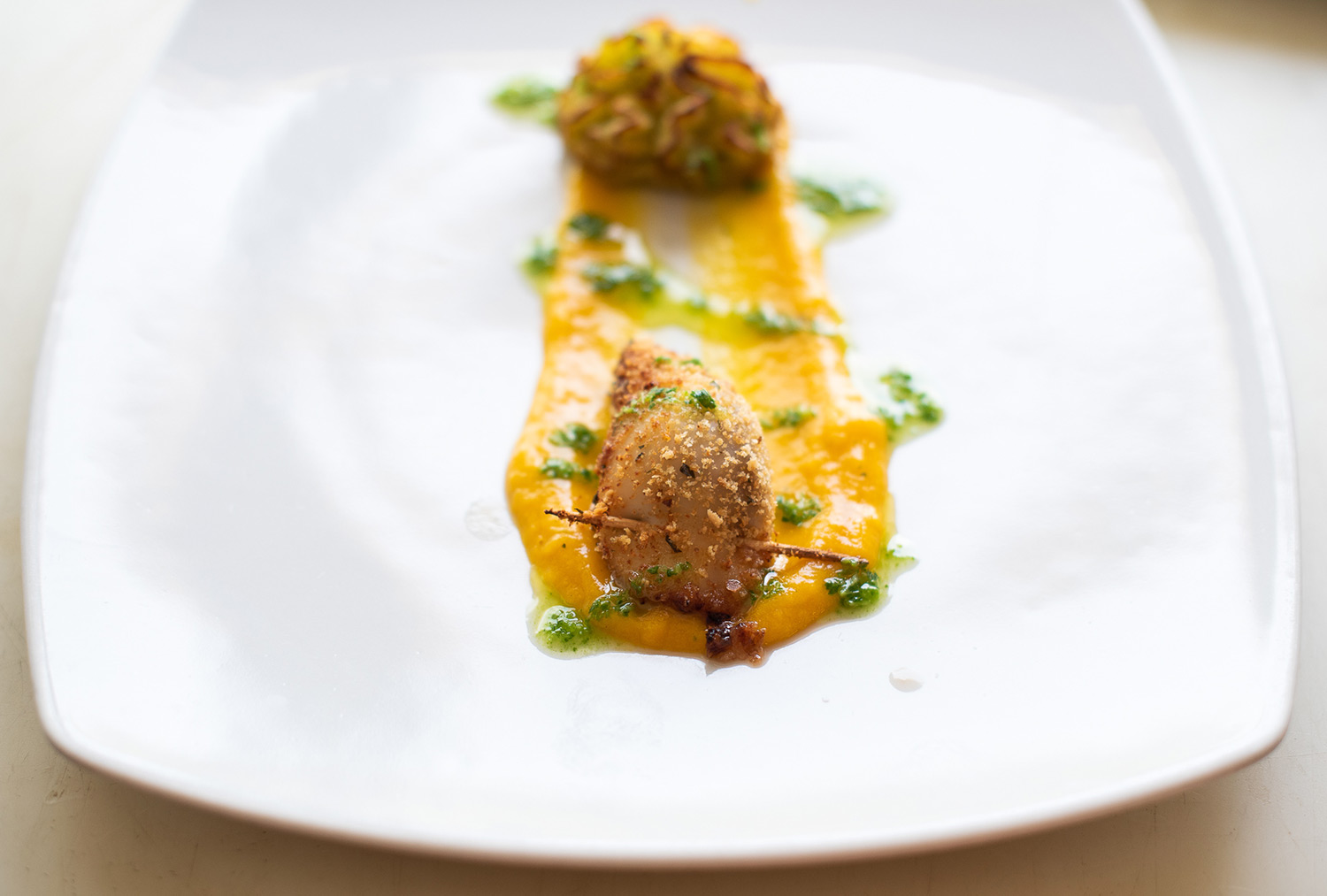 Calamaro ripieno gratinato con stecchino su crema arancione e salsa verde, piatto bianco quadrato da Lo Scoglio